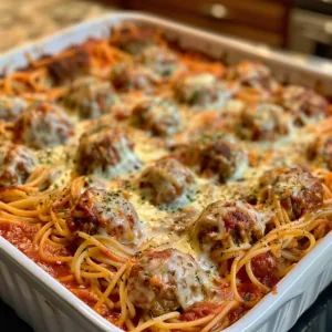 Baked meatball spaghetti served in a dish, topped with cheese and herbs.